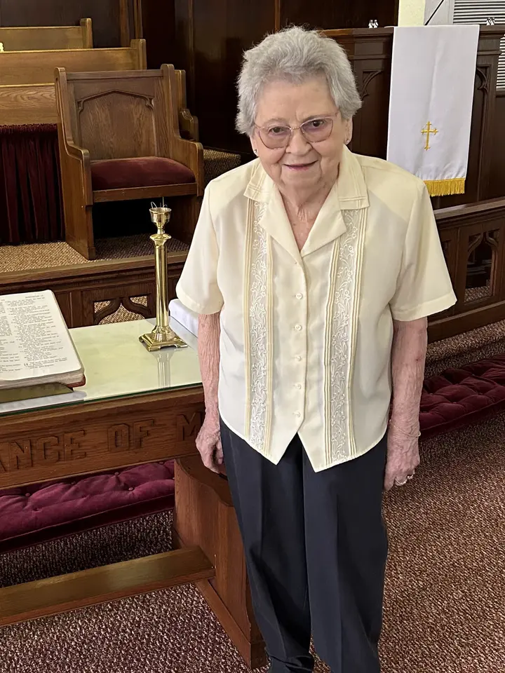 A longtime member standing at the communion rail in the sanctuary beside a brass candlestick.