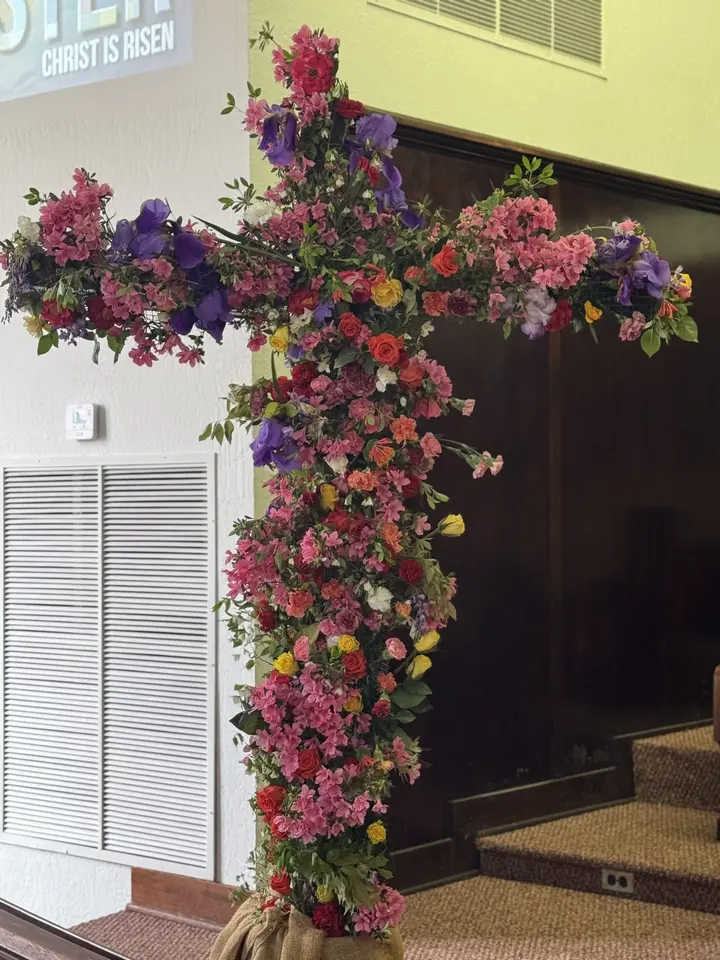 A tall wooden cross covered in red and purple flowers standing inside the sanctuary at Easter.