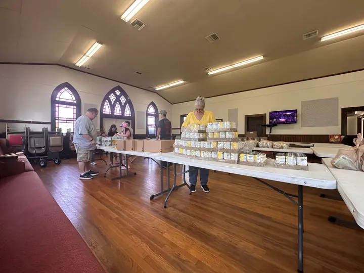 Volunteers in the fellowship hall packing brown grocery sacks at long tables for the food pantry.