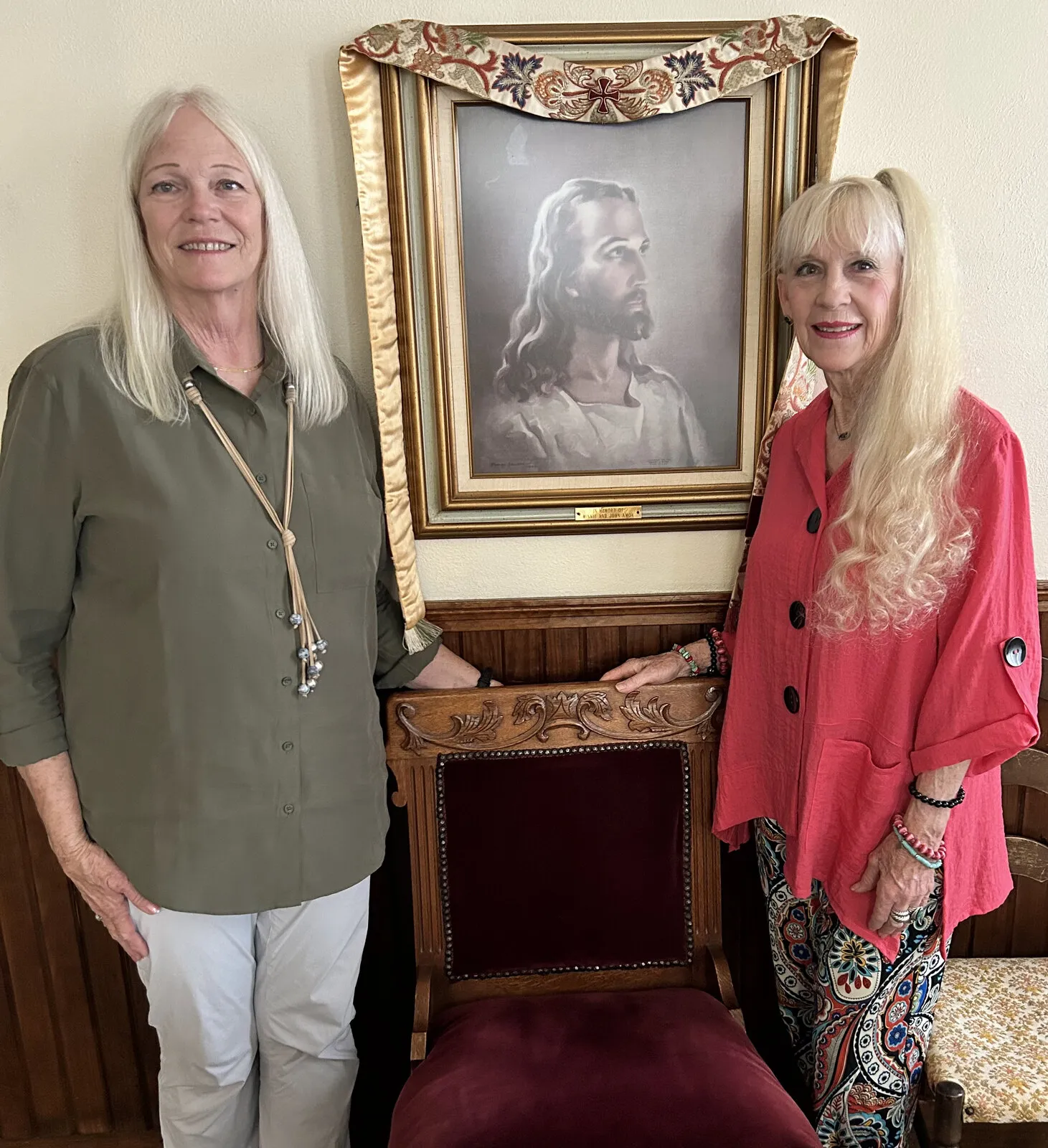 Two members standing beside a framed portrait of Christ in the sanctuary.