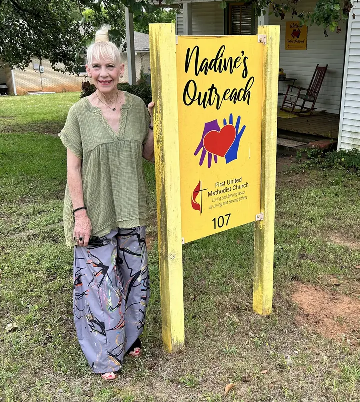 A volunteer beside the yellow 'Nadine's Outreach' yard sign outside the ministry house.