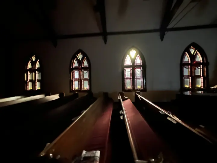 The empty sanctuary nave with wooden pews and arched stained-glass windows glowing in afternoon light.