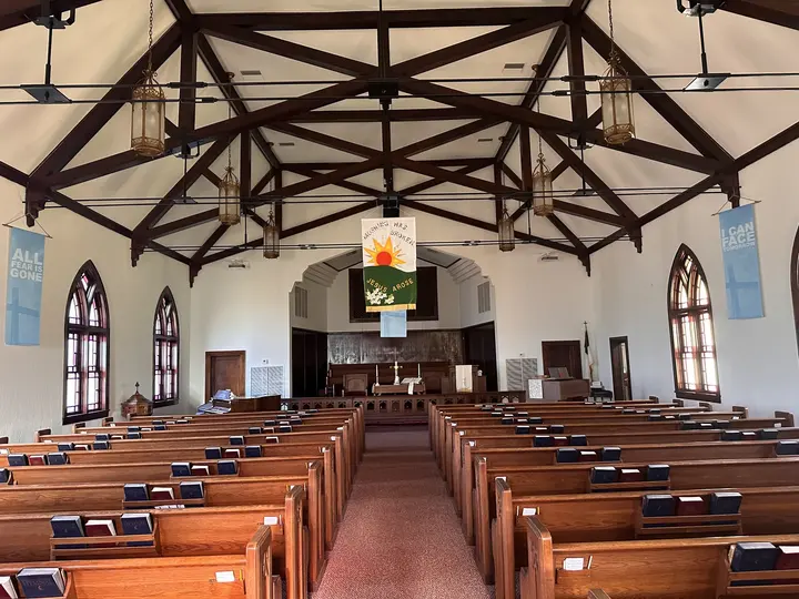 Long view down the center aisle of the sanctuary toward the chancel, beneath an open timber-vaulted ceiling.