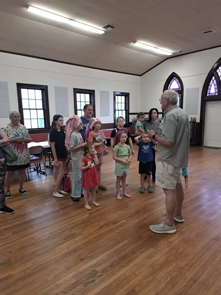 A man speaking to a group of children and families gathered in the fellowship hall at Vacation Bible School.